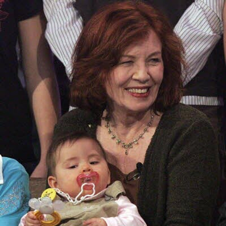 A red-haired middle-aged woman smiles with a baby holding a pacifier.